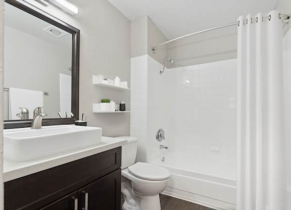 Model Bathroom with Dark Wood Cabinets, Wood-Style Flooring and Shower/Tub at Horizon Apartments located in Santa Ana, CA.