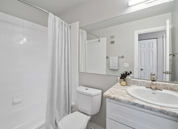 Model Bathroom with Bathtub/Shower, Wood-Style Flooring & White Cabinets at Waterfront Apartments in Lakewood, CO.
