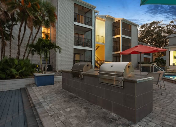 Outdoor BBQ Area with Furniture and Pool View at Haven at Water's Edge Apartments in Tampa, FL.