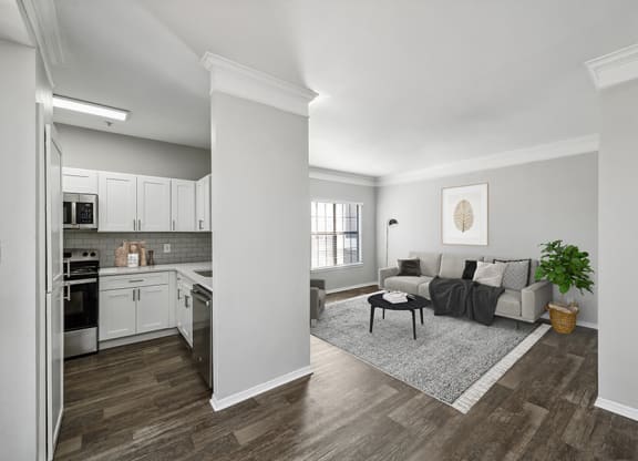 Model Kitchen with White Cabinets, Wood-Style Flooring and View of Living Room at Bridges at Oakbend Apartments located in Lewisville, TX.