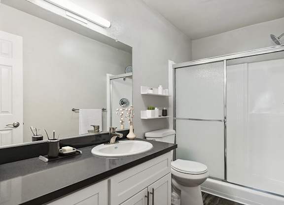 Model Bathroom with White Cabinets, Wood-Style Flooring and Shower at Madison Park Apartments located in Anaheim, CA.