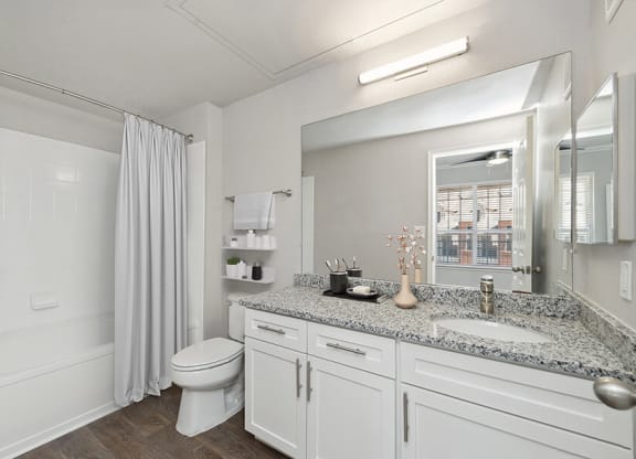 Model Bathroom with White Cabinets, Wood-Style Flooring and Shower/Tub at Chapel Hill Apartments in Lewisville, TX.