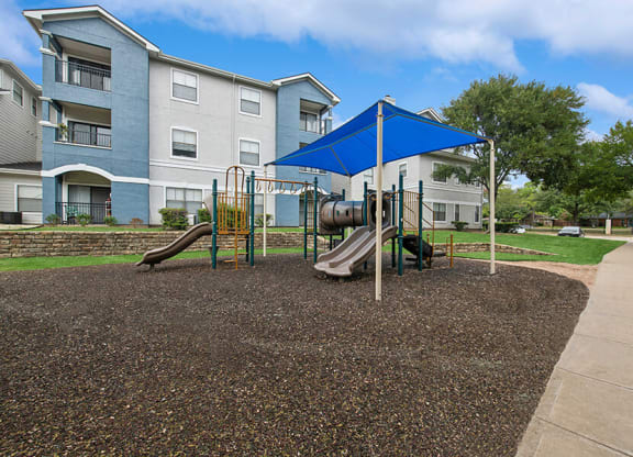Community Playground with Slide and Blue Canopy at Hidden Creek Apartments located in Lewisville, TX.