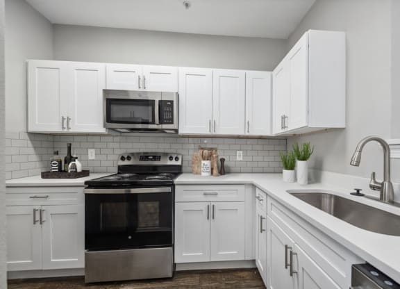 3-Bedroom Apartments in Lewisville, TX - Bridges at Oakbend - Kitchen With White Cabinets, Tile Backsplash, Stainless-Steel Appliances, Range With Microwave, And Double Sink With Sleek Faucet.