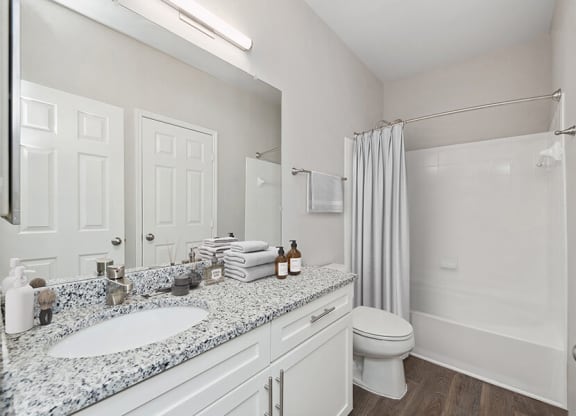 Model Bathroom with White Cabinets, Wood-Style Flooring and Shower/Tub at Chapel Hill Apartments in Lewisville, TX.