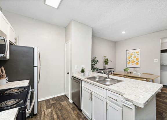 Model Kitchen with White Cabinets and Wood-Style Flooring with View of Dining Room at Dallas North Park Apartments in Dallas, TX.