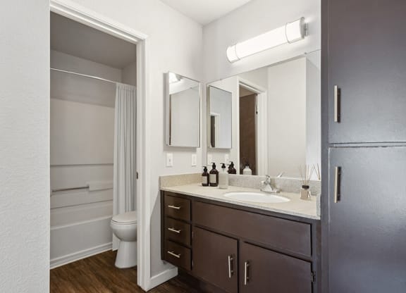 Model Bathroom with Dark Wood Cabinets, Wood-Style Flooring and Shower/Tub at Creek at 2645 Apartments located in Sacramento, CA.