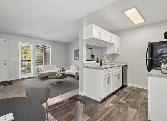 Model Kitchen with White Cabinets and Wood-Style Flooring with View of Dining/Living Room Area at Stillwater Apartments in Glendale, AZ.