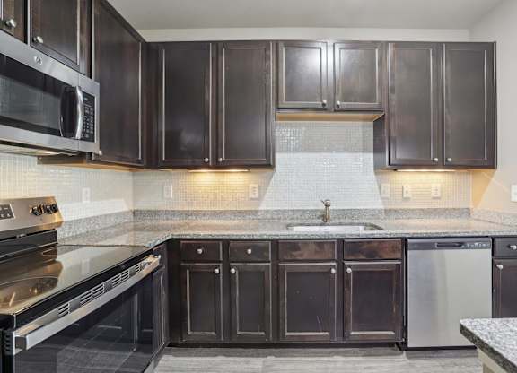 Model kitchen with dark brown cabinets and stainless steel appliances.