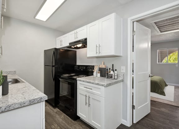 Model Kitchen with White Cabinets and Wood-Style Flooring with Bedroom Entrance at Stillwater Apartments in Glendale, AZ.