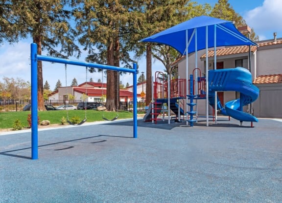 Community Playground with a Slide, Swing Set and Blue Canopy at Creek 2645 Apartments in Sacramento, CA.