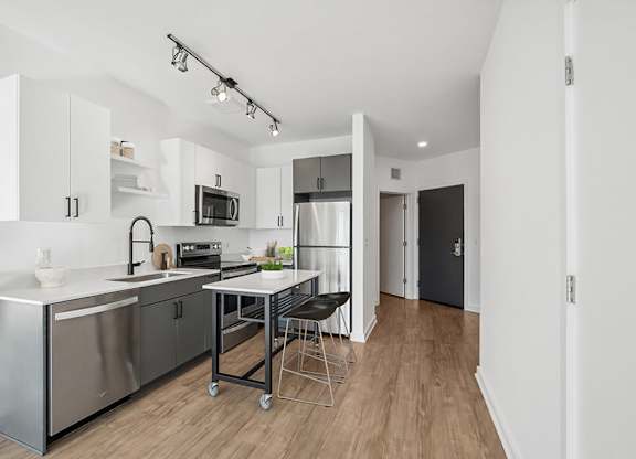 Model Kitchen with Dark Cabinets, Wood-Style Flooring and View of Living Room at Stella Apartments located in New Carrollton, MD.
