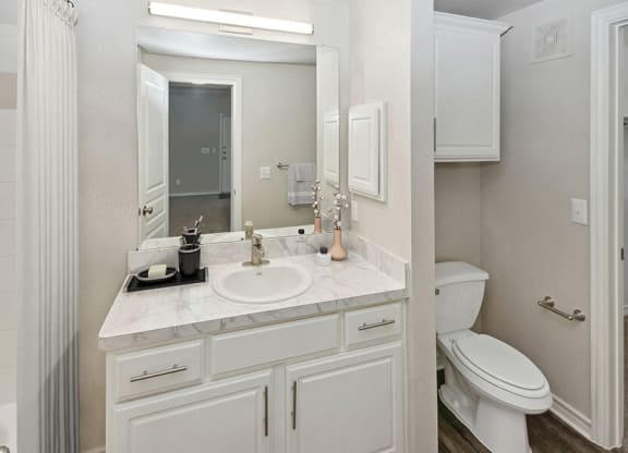 Model Bathroom with White Cabinets and Wood-Style Flooring at Belmont at Duck Creek Apartments in Garland, TX.