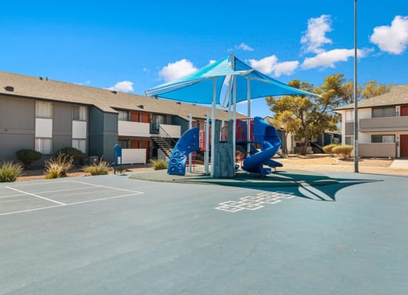 Pet-Friendly Apartments in West Las Vegas, NV - Accent on Rainbow - Courtyard Playground With Shade Canopy, Blue Slide, Painted Game Court, And Nearby Apartment Buildings