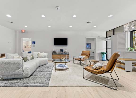 A living room with a grey sofa, a brown chair, and a TV mounted on the wall.