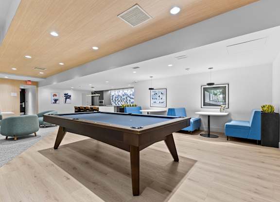 A room with a pool table and blue chairs.