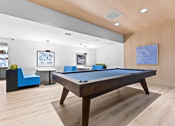 A pool table is in the middle of a room with a blue chair and a TV.