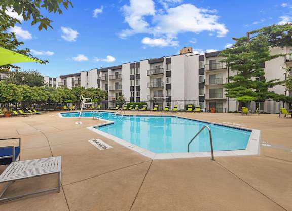 A swimming pool surrounded by a concrete patio and apartment buildings.