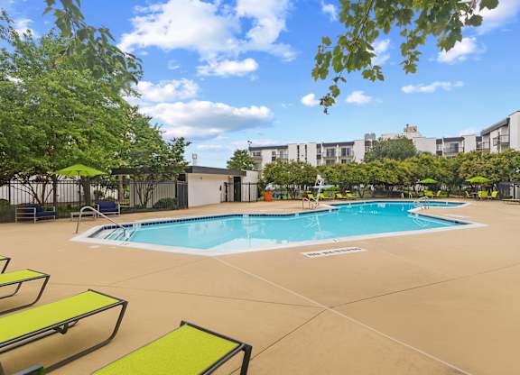 A large outdoor swimming pool surrounded by sun loungers and trees.