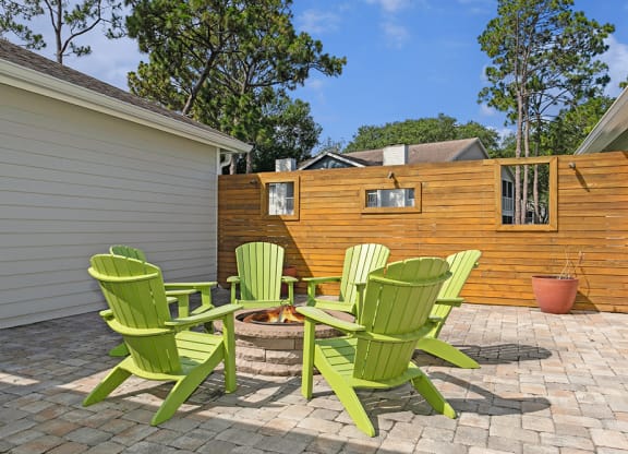 Fire pit with 4 green adirondack chairs on a brick patio at Retreat at Crosstown Apartments