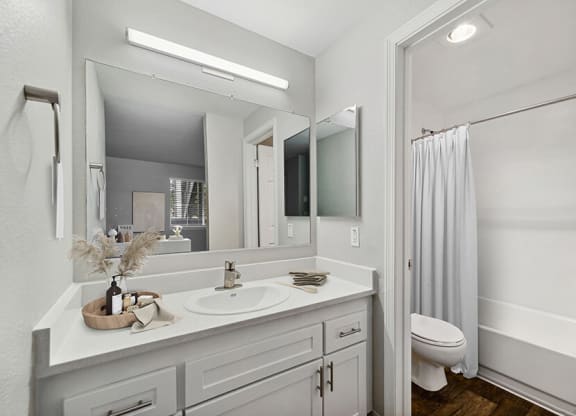 Model Bathroom with White Cabinets, Wood-Style Flooring and Shower/Tub at Central Flats Apartments in Kent, WA.