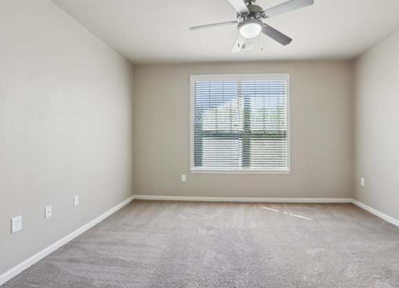 Model bedroom with a ceiling fan and a window with blinds.