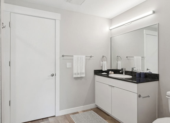 Model Bathroom with Wood-Style Flooring, White Cabinets & Shower/Tub at Seven Skies Apartments located in Sandy, UT.
