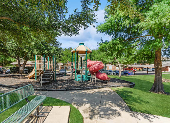 Community Playground with Two Slides and Bench Area at Belmont at Duck Creek Apartments in Garland, TX.