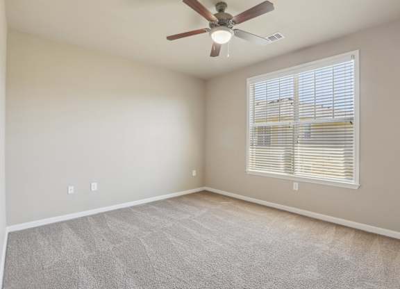 Model bedroom with a ceiling fan and a window with blinds.