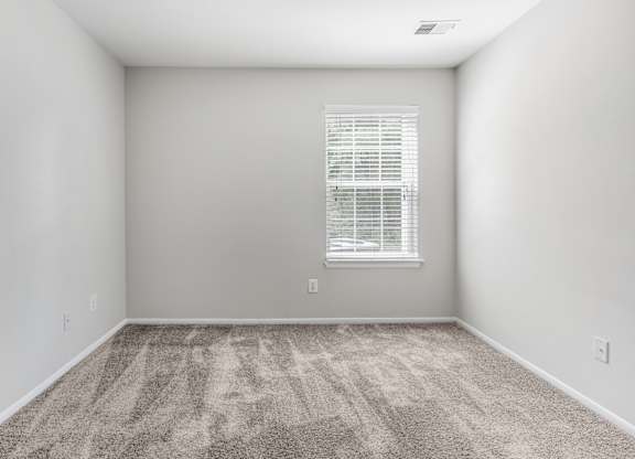 A room with a carpeted floor and a window with blinds.