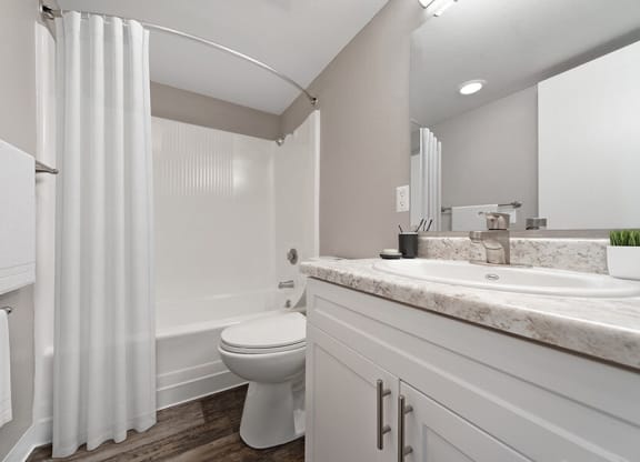Model Bathroom with White Cabinets, Wood-Style Flooring and Shower/Tub at Bridges at 9 Mile Station Apartments in Denver, CO.