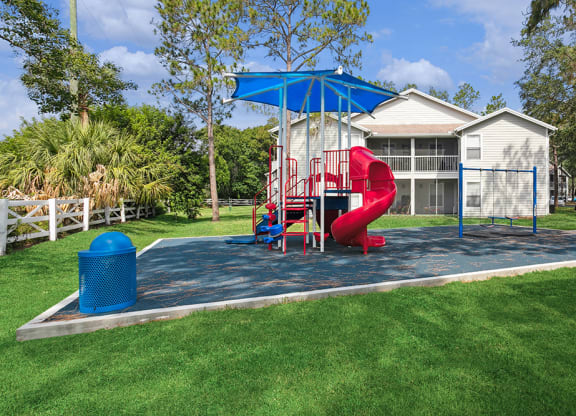 Community playground with a red slide and sun cover at Retreat at Crosstown Apartments