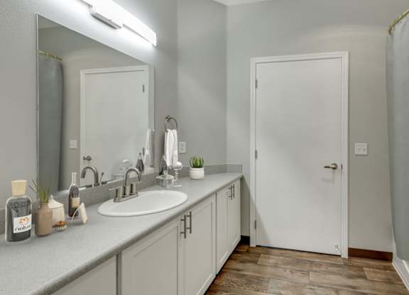 Model Bathroom with White Cabinets, Wood-Style Flooring and Shower/Tub at Landings at Morrison Apartments located in Gresham, OR.