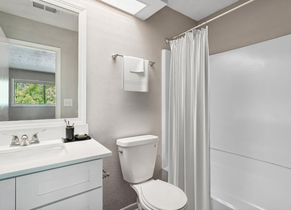 Model Bathroom with White Cabinets, Wood-Style Flooring & Shower/Tub at Lakeside Retreat Apartments located in Peachtree Corners, GA.