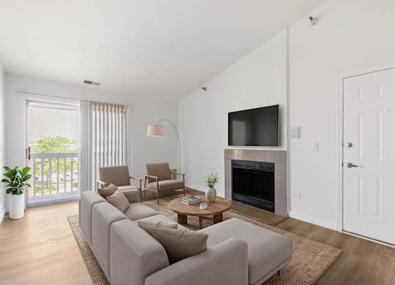 Model living room with a grey sofa, a wooden coffee table, a fireplace, and a sliding glass door leading to a balcony.