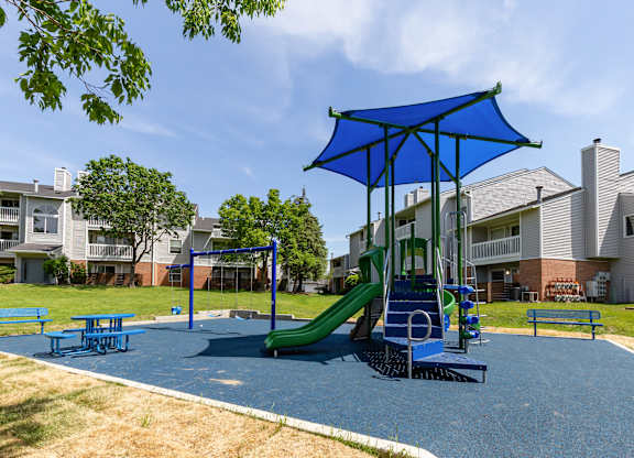 Community playground with a blue umbrella and a green slide.