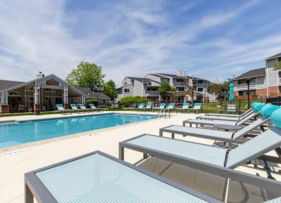 Community pool with sun loungers and a table in the foreground with apartment buildings in the background.