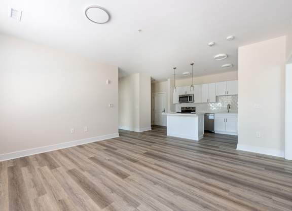 A spacious room with wooden flooring and a kitchen area in the background.