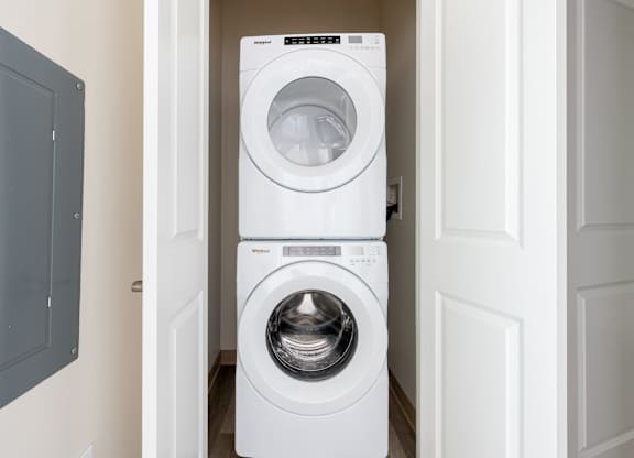 A white washing machine is stacked on top of another white washing machine in a narrow hallway.