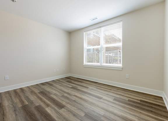 A room with wooden flooring and a window with blinds.