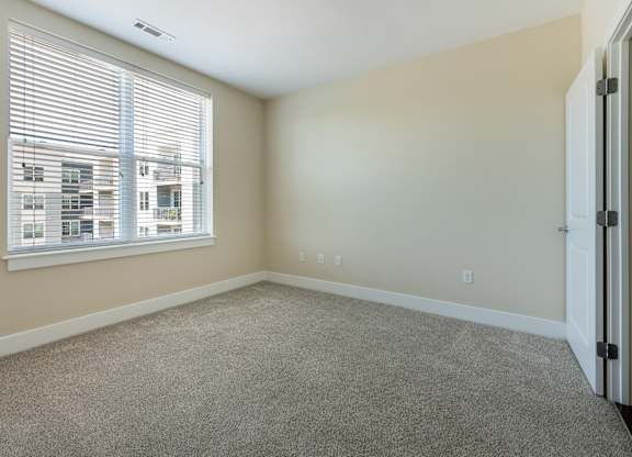 A room with a carpeted floor and a window with blinds.