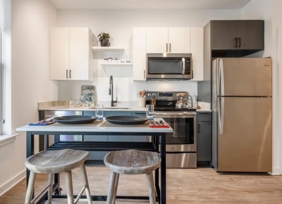 Model kitchen with stainless steel appliances and a counter with two stools