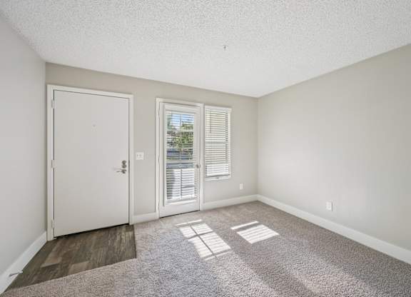 Model living room with a white door, a window with blinds, and a carpeted floor.