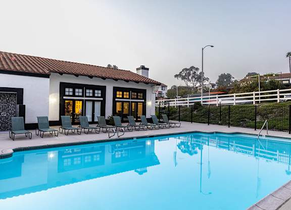 A swimming pool in front of a house with a black fence.