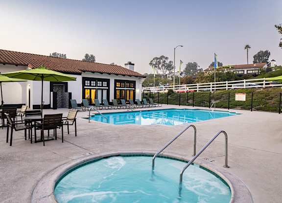 A pool with a hot tub and chairs in front of a house.