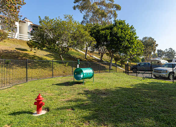 A green barrel sits on a grassy area next to a red fire hydrant.