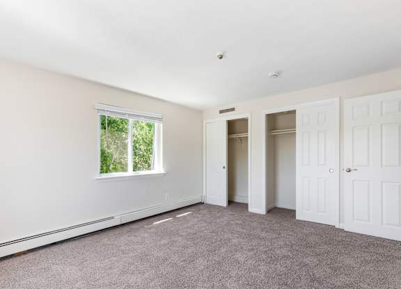 A room with white walls and a window with a view of trees.