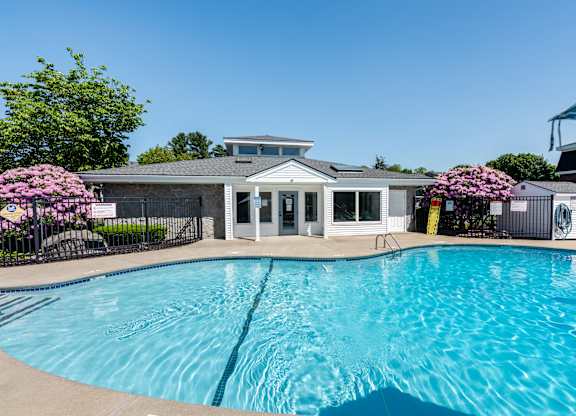 A swimming pool in front of a building with a black fence and pink flowers.