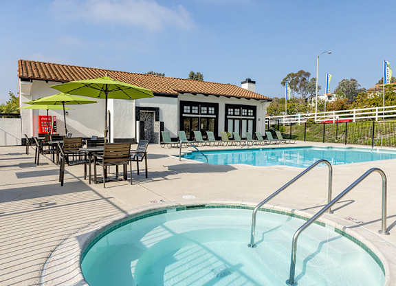 A pool with a ladder and a table with chairs and an umbrella outside a building.