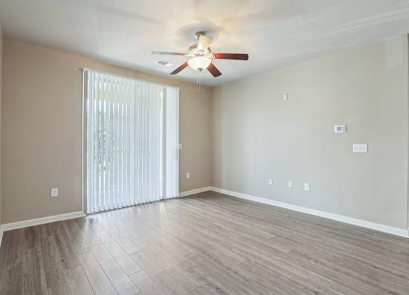 Model living room with a ceiling fan and sliding glass doors.